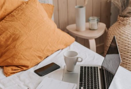 Portable Computer - From above of open netbook with black screen and cup of coffee with smartphone and notebook placed on crumpled bed sheet in bedroom with big vase on floor