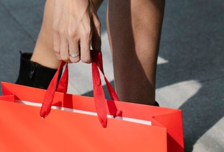 Custom Cooling - From above of crop faceless stylish female buyer in mini skirt and boots putting red paper bag on ground while standing on street after shopping